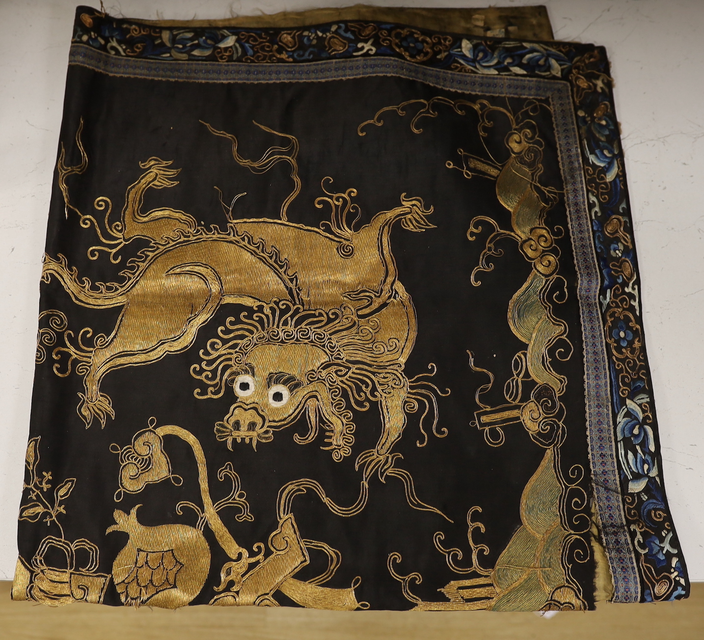 A 19th century Chinese dark blue ground panel, gilt thread embroidered with a pair of celestial dragons flying amongst precious objects, beneath a frieze, 95 x 95cm